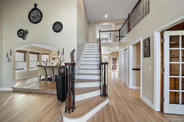 stairs with a towering ceiling, baseboards, arched walkways, and wood finished floors