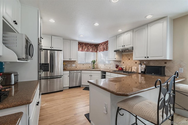 kitchen with appliances with stainless steel finishes, light wood-style floors, white cabinetry, a sink, and a peninsula