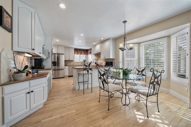 dining area with light wood finished floors, baseboards, a chandelier, and a textured ceiling