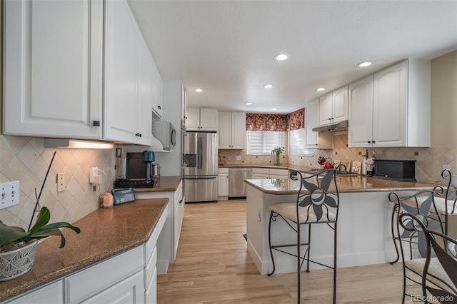 kitchen featuring appliances with stainless steel finishes, a breakfast bar, a peninsula, under cabinet range hood, and a sink