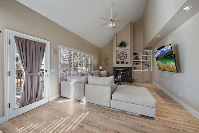 living area featuring a fireplace, ceiling fan, wood finished floors, high vaulted ceiling, and baseboards