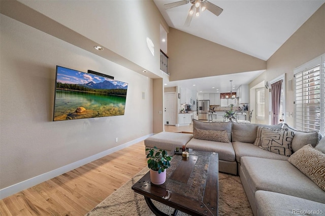 living room featuring high vaulted ceiling, light wood-style flooring, baseboards, and ceiling fan