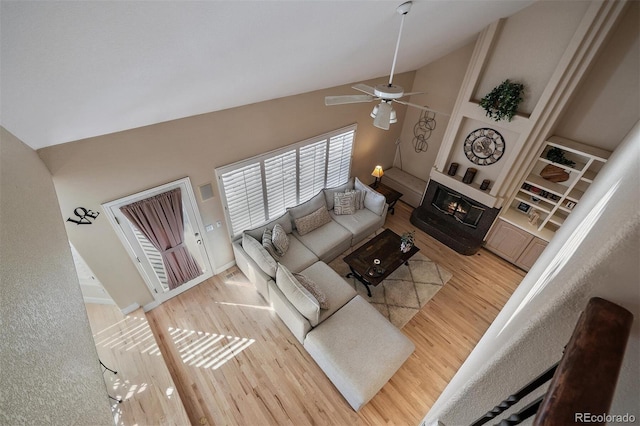 living room featuring ceiling fan, high vaulted ceiling, wood finished floors, built in features, and a glass covered fireplace