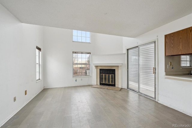 unfurnished living room with light wood-style floors, a fireplace, baseboards, and a textured ceiling