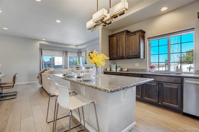 kitchen featuring a kitchen breakfast bar, sink, stainless steel dishwasher, decorative light fixtures, and light stone counters