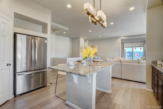 kitchen with stainless steel refrigerator, hanging light fixtures, light stone counters, light hardwood / wood-style floors, and a breakfast bar