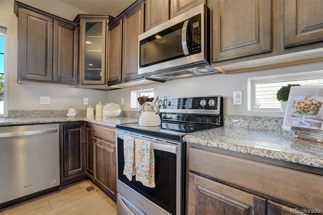 kitchen featuring dark brown cabinetry, light stone counters, light wood-type flooring, and appliances with stainless steel finishes