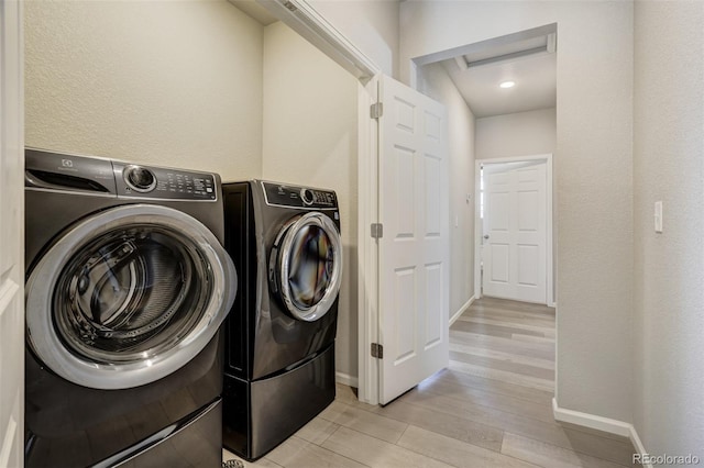 clothes washing area with washing machine and clothes dryer and light hardwood / wood-style floors