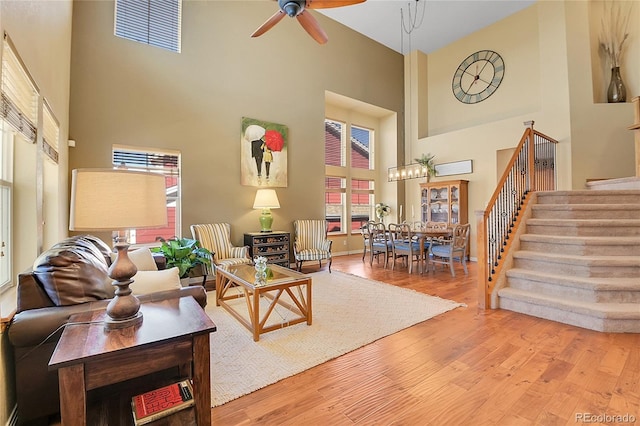 living area with a towering ceiling, stairs, a ceiling fan, and wood finished floors