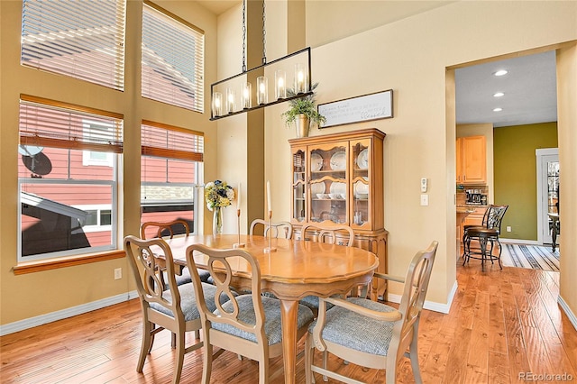 dining area with light wood-type flooring, a notable chandelier, recessed lighting, a high ceiling, and baseboards