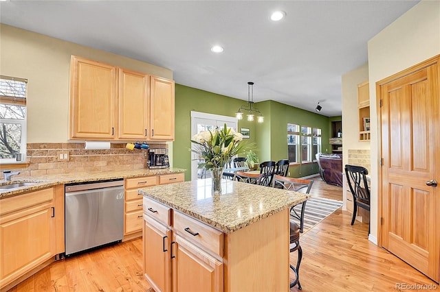 kitchen featuring a kitchen breakfast bar, stainless steel dishwasher, a healthy amount of sunlight, and light brown cabinetry