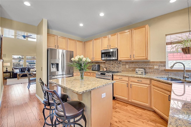 kitchen featuring a breakfast bar, light brown cabinetry, a sink, plenty of natural light, and stainless steel appliances