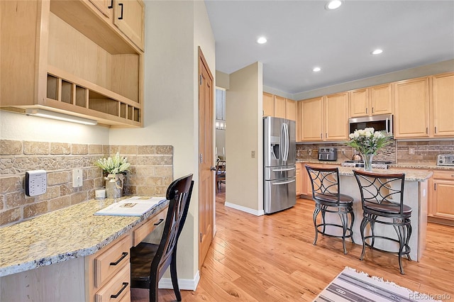 kitchen with a breakfast bar, light brown cabinets, built in desk, appliances with stainless steel finishes, and light wood finished floors