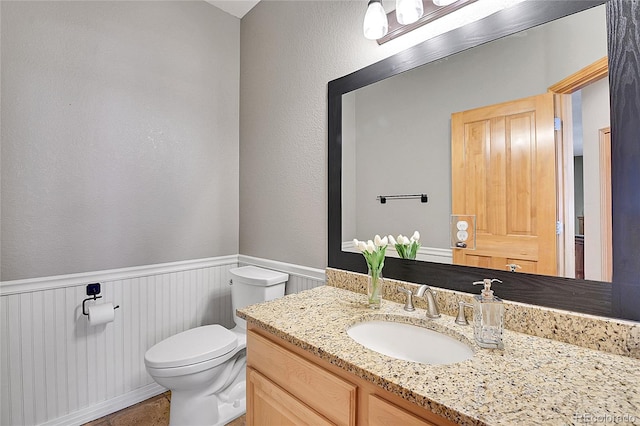 half bathroom with wainscoting, toilet, and vanity