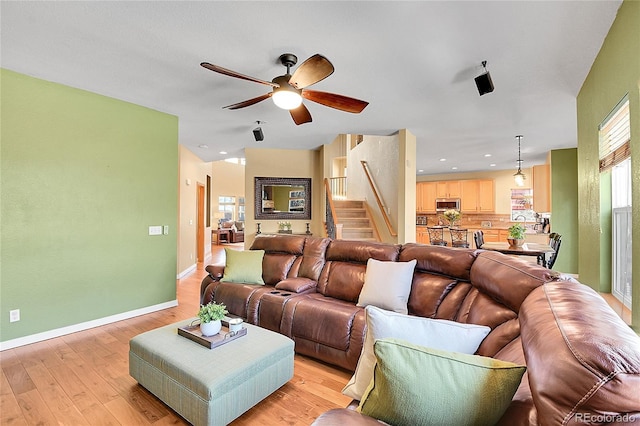 living room featuring light wood-type flooring, stairway, baseboards, and a ceiling fan