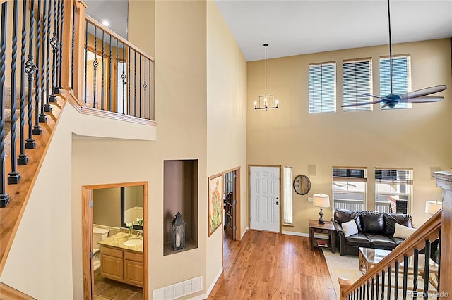 foyer entrance featuring ceiling fan with notable chandelier, wood finished floors, visible vents, and a healthy amount of sunlight