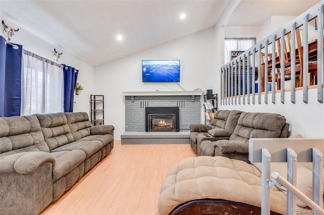 living room with plenty of natural light, a brick fireplace, vaulted ceiling, and wood finished floors