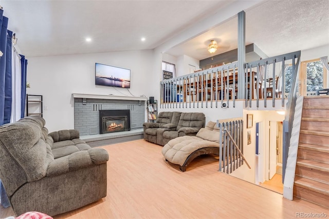 living area with wood finished floors, stairs, vaulted ceiling, a brick fireplace, and recessed lighting