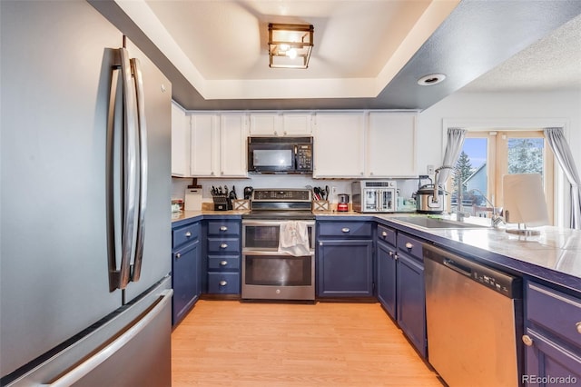 kitchen featuring a raised ceiling, appliances with stainless steel finishes, light wood-style floors, white cabinetry, and blue cabinets