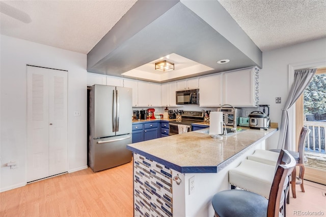 kitchen with light wood-style flooring, a peninsula, white cabinets, appliances with stainless steel finishes, and blue cabinetry