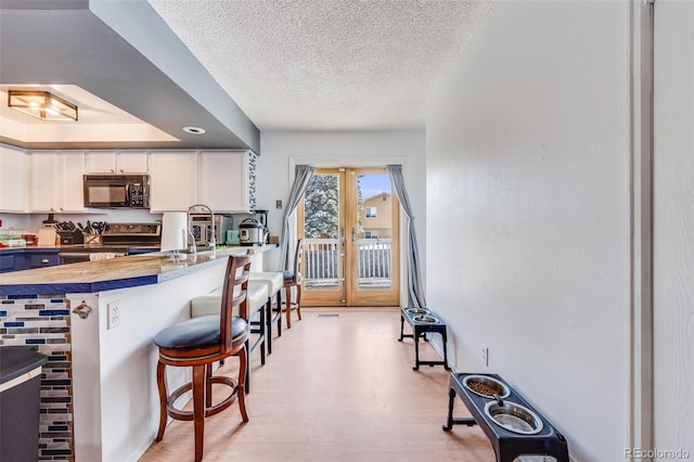 kitchen featuring a breakfast bar, light countertops, white cabinetry, stainless steel range with electric cooktop, and black microwave