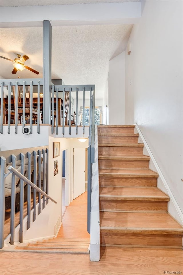 staircase with ceiling fan, a textured ceiling, and wood finished floors