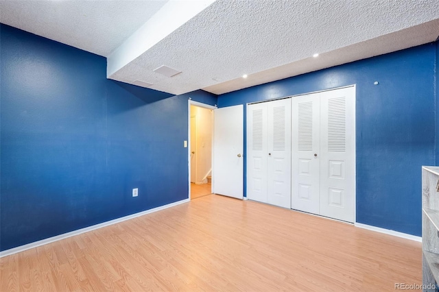 unfurnished bedroom with a closet, baseboards, a textured ceiling, and light wood finished floors