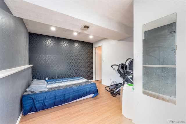 bedroom with recessed lighting, an accent wall, wood finished floors, visible vents, and wallpapered walls