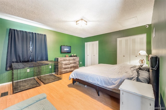 bedroom featuring two closets, visible vents, attic access, a textured ceiling, and wood finished floors