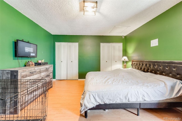 bedroom featuring attic access, baseboards, wood finished floors, a textured ceiling, and two closets