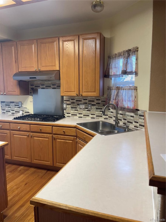 kitchen with backsplash, stainless steel gas stovetop, sink, and light hardwood / wood-style flooring