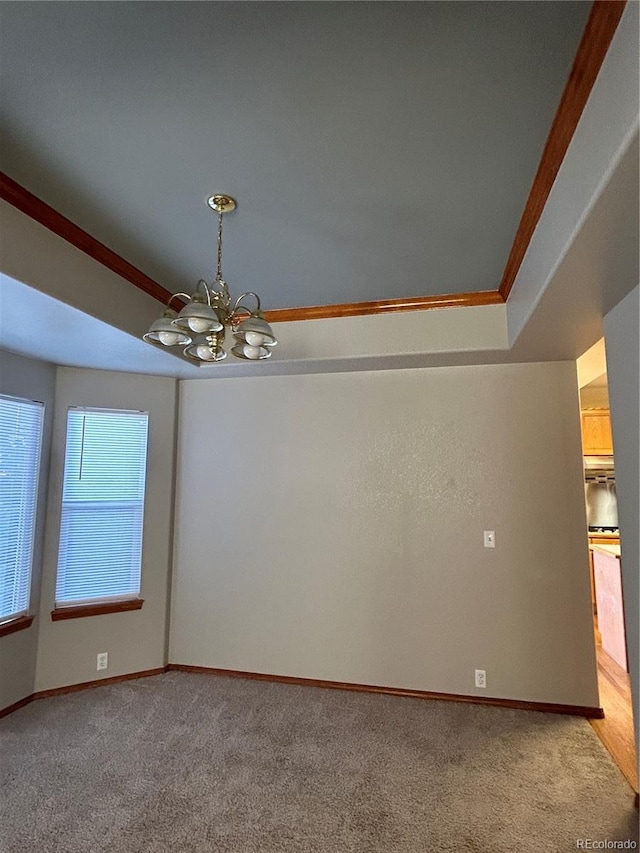 carpeted empty room with a raised ceiling, an inviting chandelier, and ornamental molding