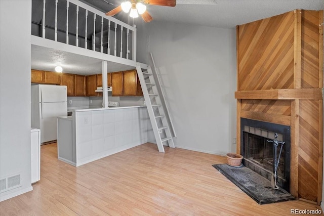 unfurnished living room featuring a fireplace with raised hearth, ceiling fan, lofted ceiling, visible vents, and light wood-type flooring