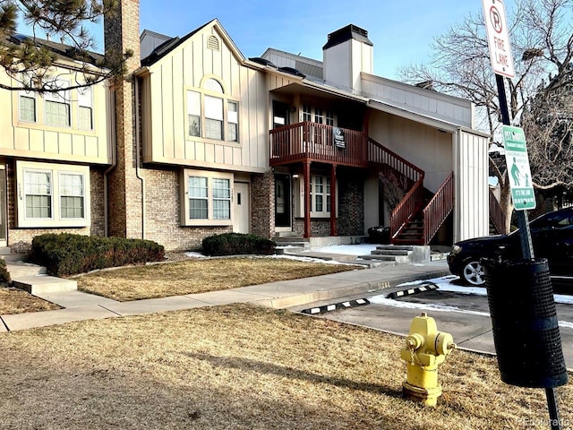 view of front of house with a chimney, stairway, uncovered parking, board and batten siding, and brick siding