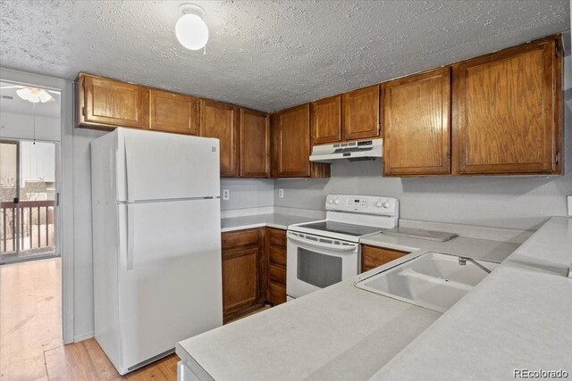 kitchen with white appliances, brown cabinets, light countertops, under cabinet range hood, and a sink