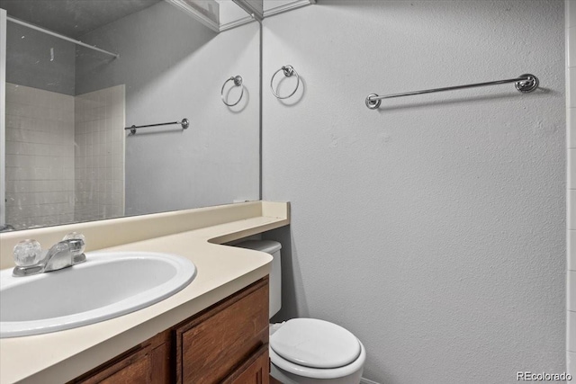 full bathroom featuring toilet, a textured wall, walk in shower, and vanity