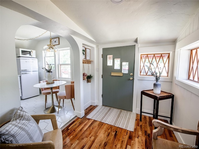 foyer entrance featuring an inviting chandelier, arched walkways, vaulted ceiling, and wood finished floors