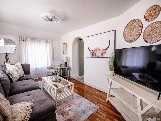 living area with arched walkways, ceiling fan, wood finished floors, baseboards, and vaulted ceiling