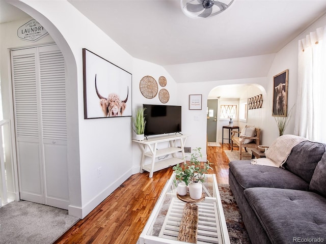 living room with arched walkways, wood finished floors, lofted ceiling, and baseboards