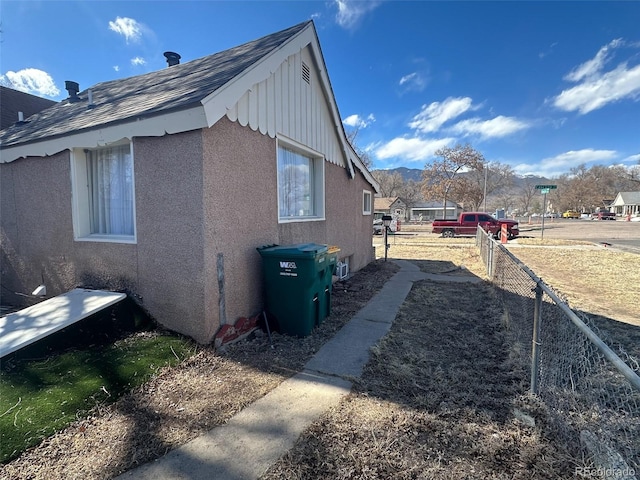 view of property exterior featuring a shingled roof, fence, and stucco siding