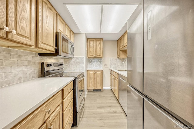 kitchen with stainless steel appliances, light hardwood / wood-style floors, sink, light brown cabinetry, and backsplash