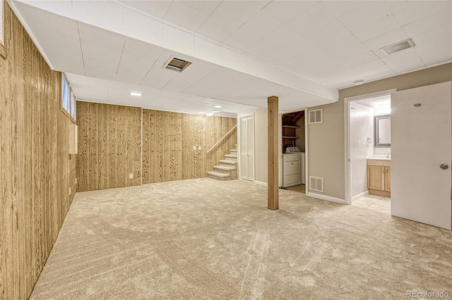 basement featuring wood walls, light colored carpet, and washer / dryer