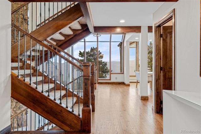 stairway featuring baseboards, beamed ceiling, and wood finished floors