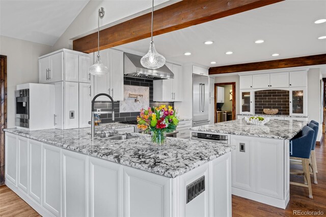 kitchen featuring wood finished floors, tasteful backsplash, white cabinetry, a sink, and wall chimney range hood