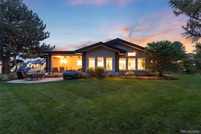 back house at dusk featuring a yard and a patio