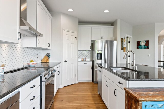 879 Quintana Ln, Erie, CO 80516 - kitchen featuring wall chimney range hood, a sink, stainless steel appliances, arched walkways, and light wood-style floors