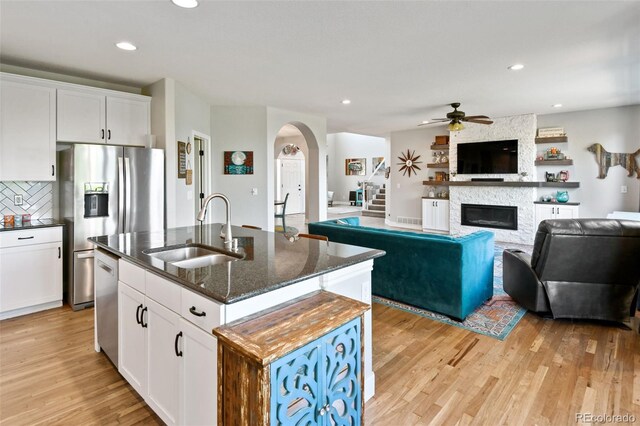879 Quintana Ln, Erie, CO 80516 - kitchen with a sink, appliances with stainless steel finishes, a fireplace, ceiling fan, and light wood-type flooring