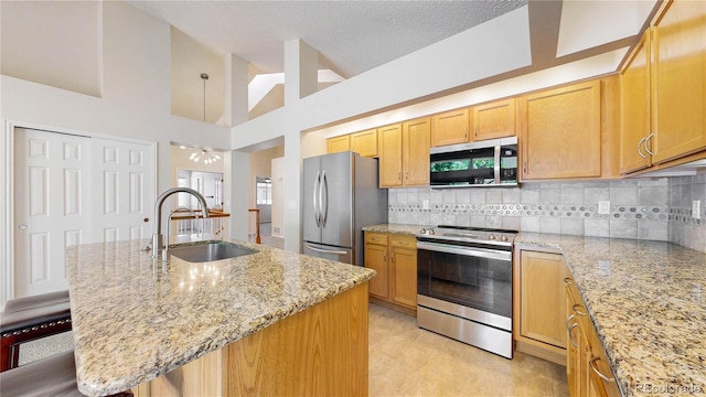 kitchen featuring stainless steel appliances, a sink, tasteful backsplash, light stone countertops, and an island with sink