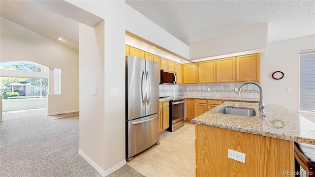 kitchen with appliances with stainless steel finishes, a sink, light stone countertops, light colored carpet, and a peninsula
