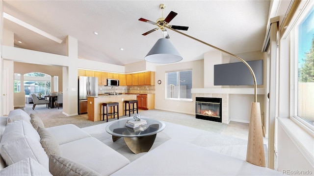 living area featuring a tile fireplace, a ceiling fan, light colored carpet, baseboards, and high vaulted ceiling
